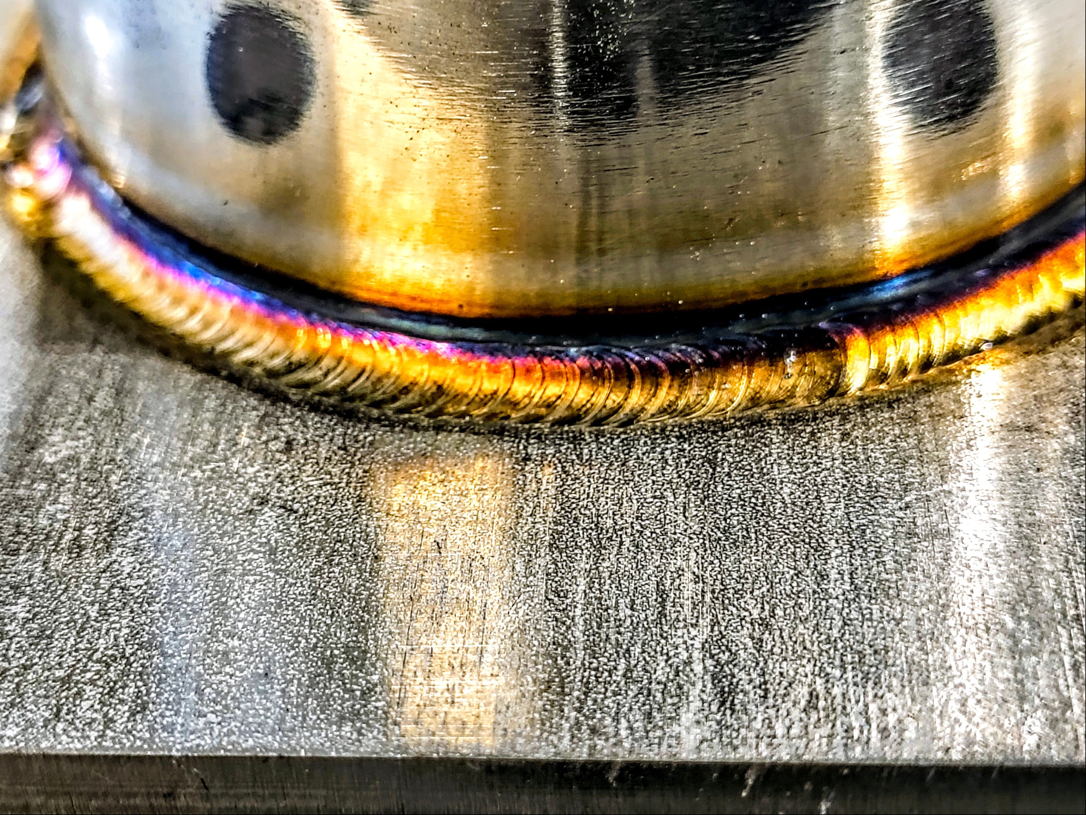Close-up of a metallic object with a rainbow-colored edge on a textured surface